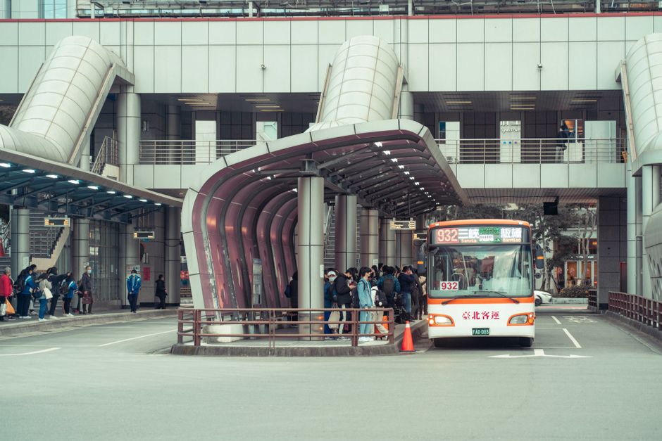 Mobilidade Urbana — Public transport bus picking up commuters at a modern urban terminal with architectural features.